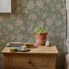 AMELIE LICHEN olive green background with pink and beige flower design used in bedroom with natural wood bedside table and plant