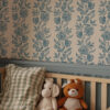 Dilys Teal Wallpaper in Bedroom beige background with dark blue flower and leaf pattern in a baby's nursery with cot and 2 teddies