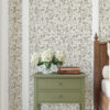Elena Light Green floral Wallpaper used on wall in bedroom with the side of the bed in view and a green bedside table with 2 books on it and a vase of cream hydrangers - just one of our home decor inpsiration ideas