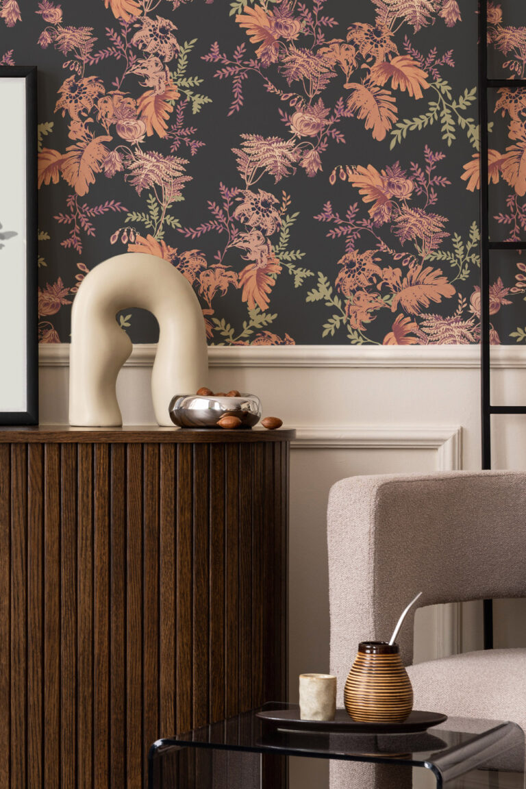 MINA MIDNIGHT wallpaper with dark background and orange, pink and green fern designs on the wall above a panelled area with a dark wood side board and chair and coffee table in front. Mina is part of our home decor collection The Series Collection. Contact Curate Space for more details