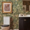 IRIS SOFT GREEN wallpaper with gold beige floral dwsign in a bathroom with a dark vanity unit and toilet and a picture on the wall with a light and mirror