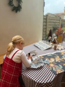 a little girl leaning over a table making christmas decorations out of left over Curate Space wallpaper