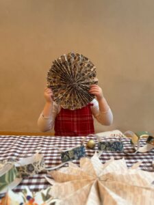a little girl holding a large Christmas Decoration in front of their face that they have just made out of leftover Curate Space Wallpaper
