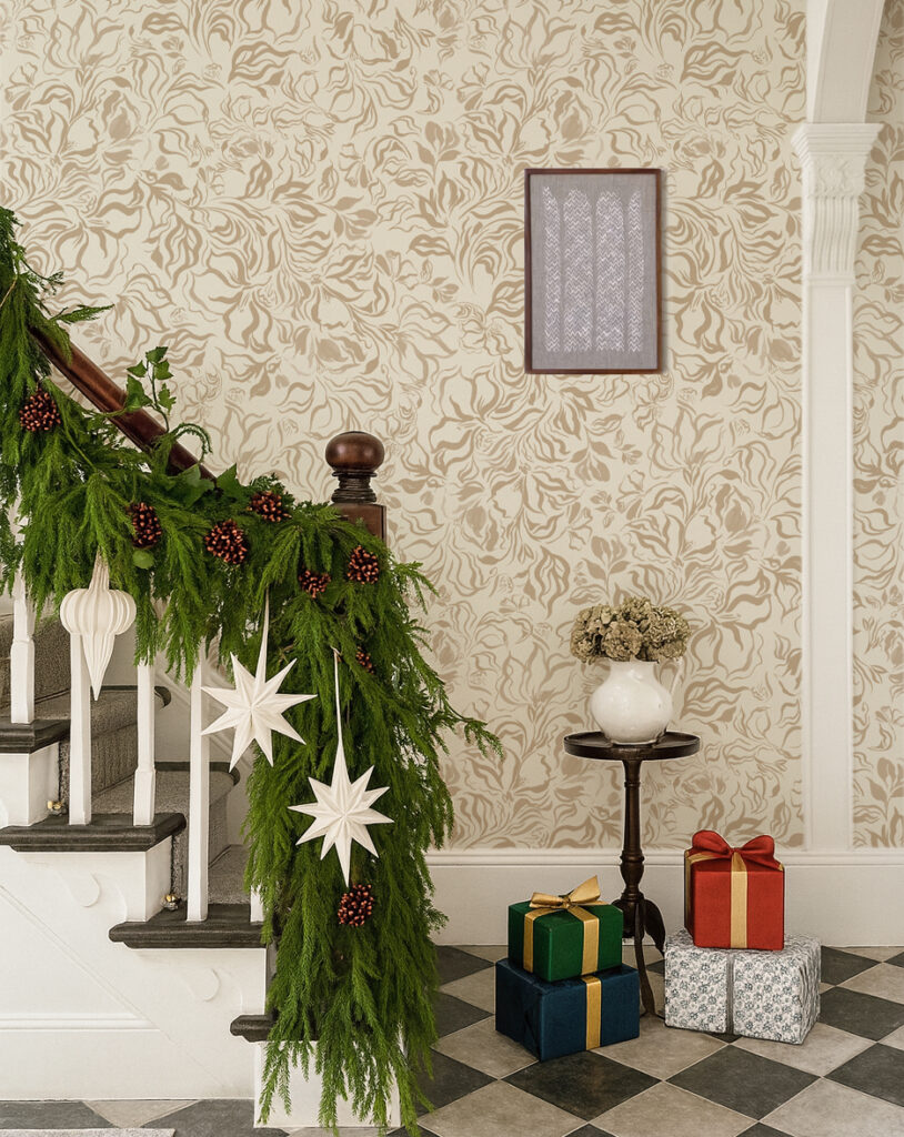 Bannister with Christmas garland and presents at the bottom with bespoke wallpaper Eva in pebble by Curate space in the background